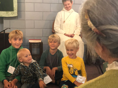 Several children sitting at front of church while proud parents and staff look on